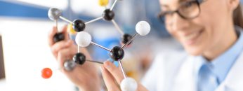 smiling scientist holding molecular model in laboratory, focus on foreground