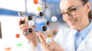 smiling scientist holding molecular model in laboratory, focus on foreground